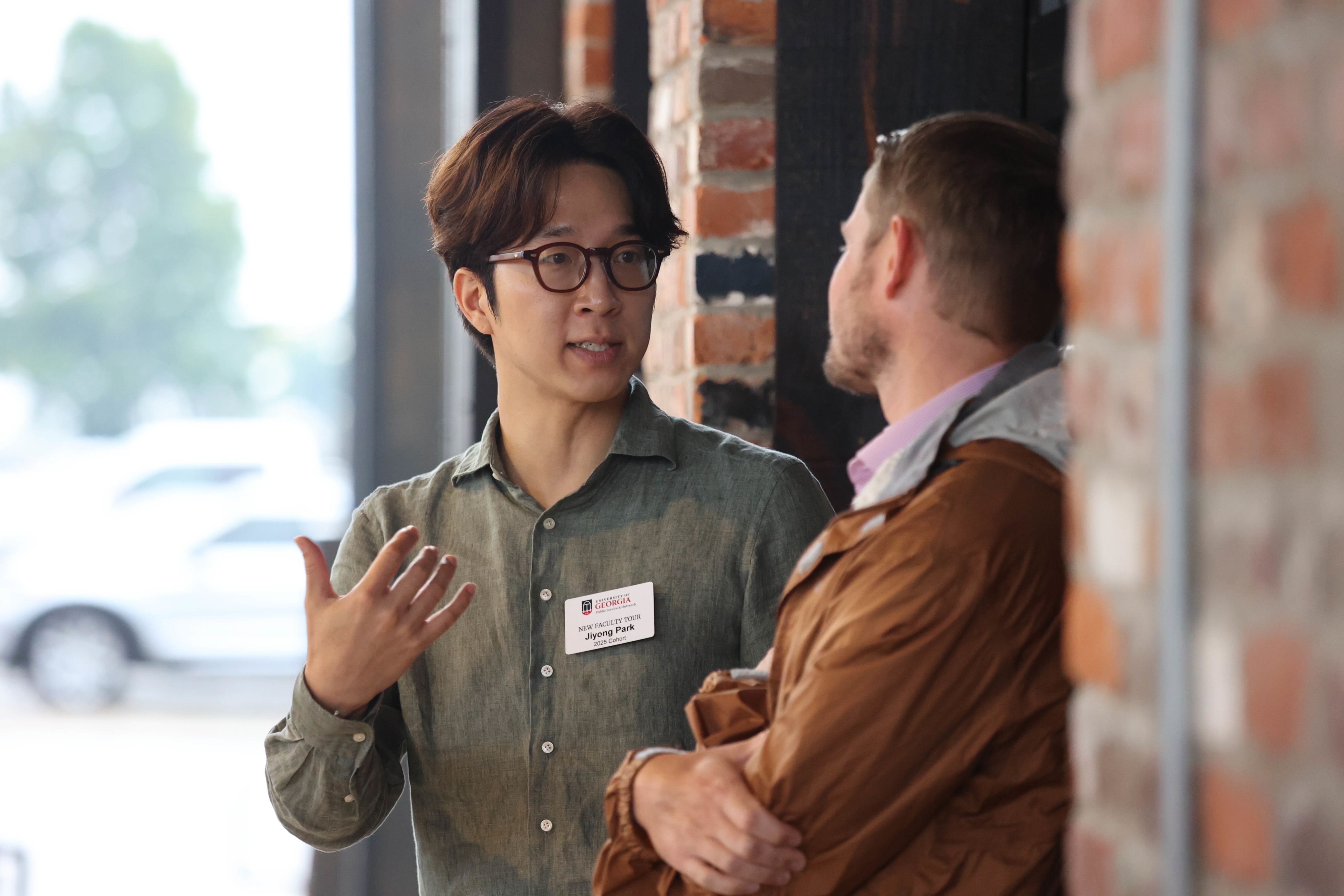 a man with glasses on UGA's New Faculty Tour talks to another male participant from the tour with a brick background